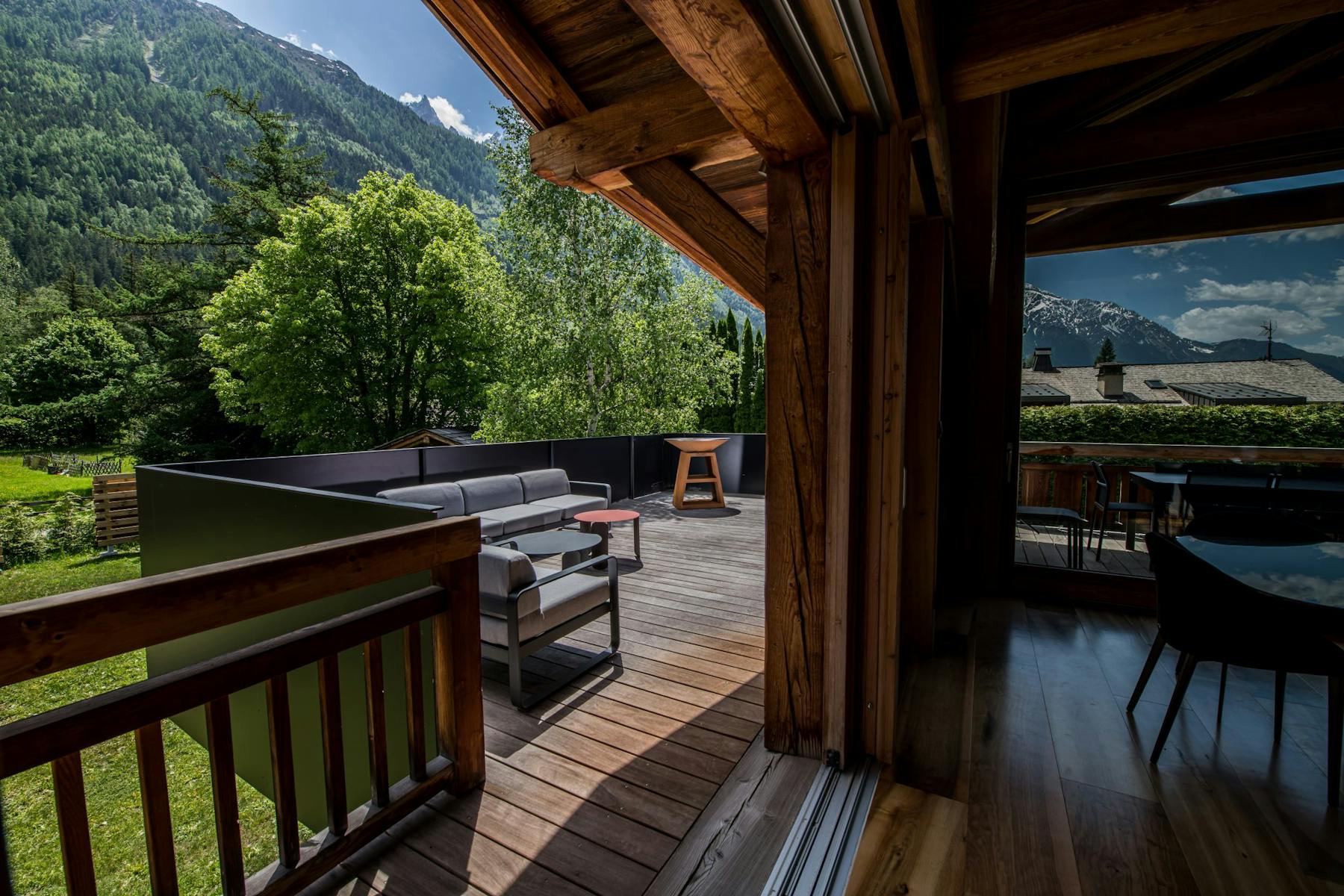 Le balcon couvert du Chalet Bonami aux Bois : salon de jardin et brasero sur un plancher en bois, forêt et sommets de la vallée de Chamonix en arrière-plan