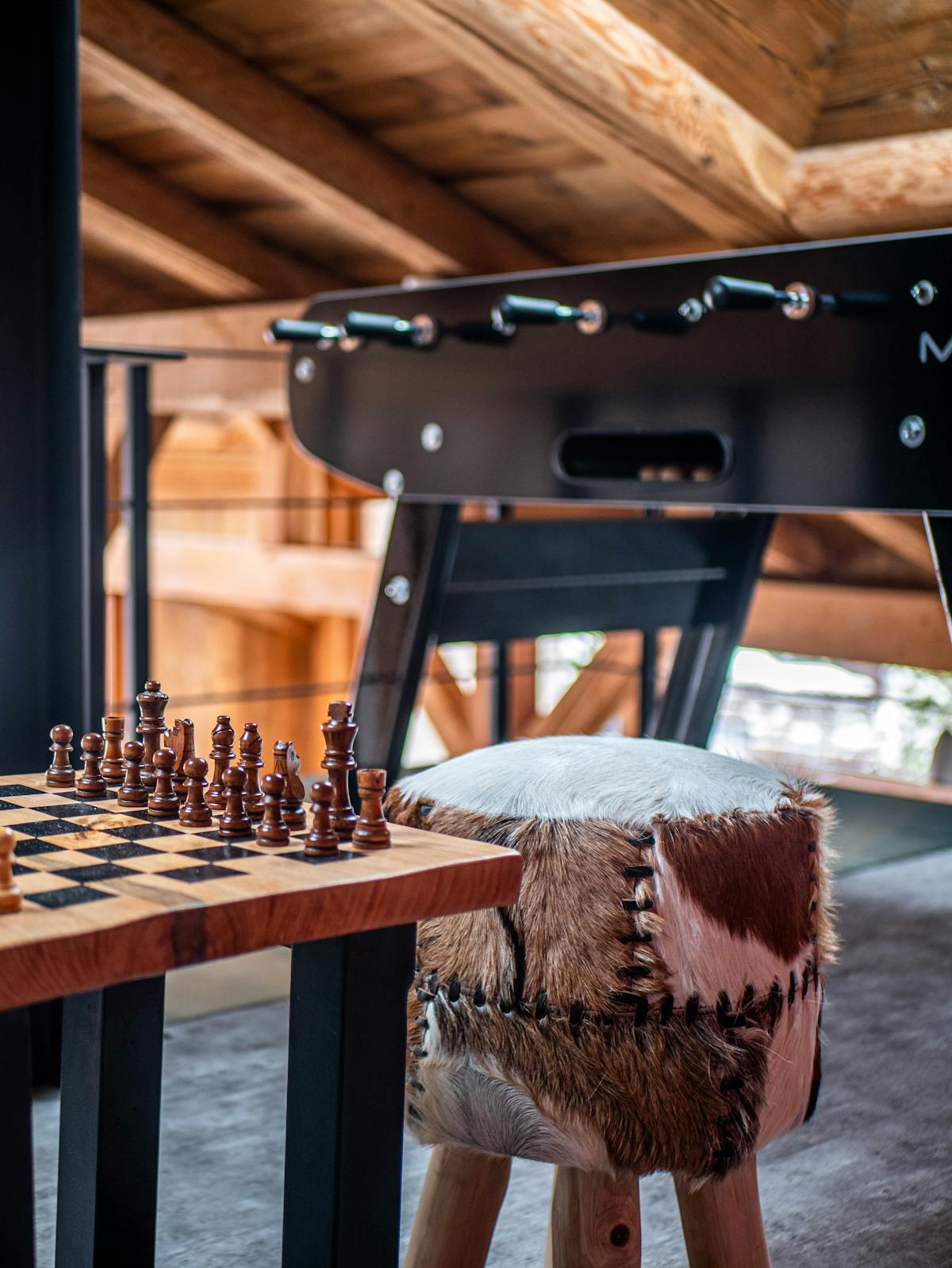 Wooden chess set and a table football in a side room of a chalet, with a hide-covered stool