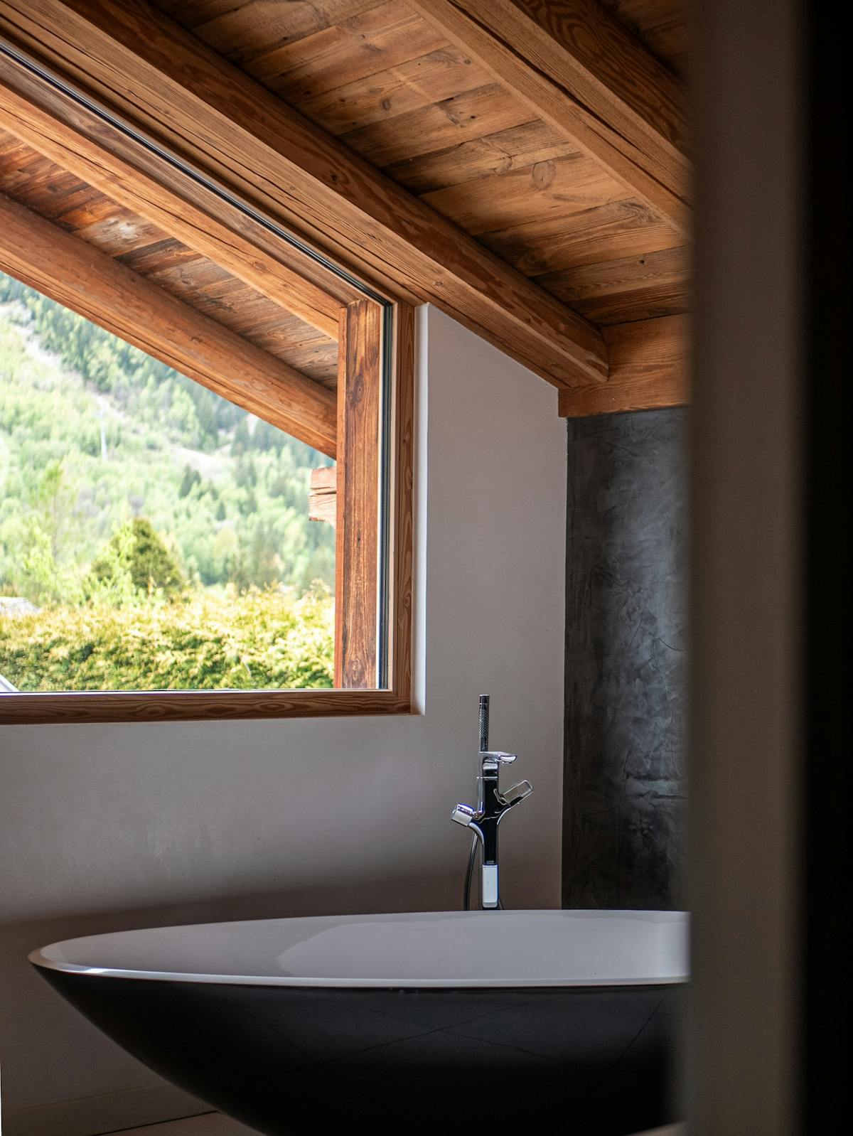 La salle de bain de la chambre Master, sous la charpente : baignoire îlot devant une fenêtre ouverte sur la forêt