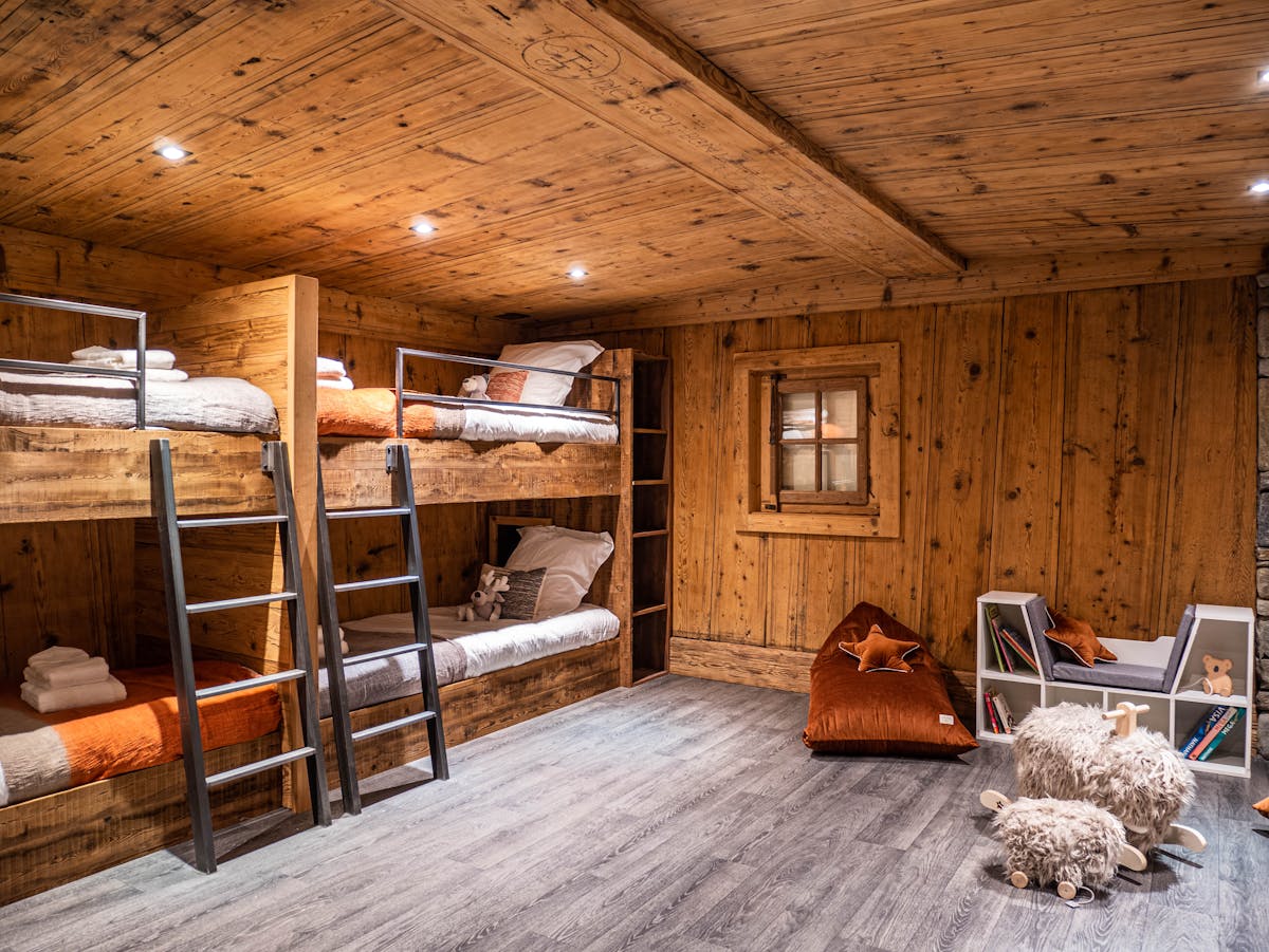 The bunk room at Chalet Bonami: two bunk beds built into the old timber with their ladders, and the reading corner of the room with its bench, bookshelf and toys